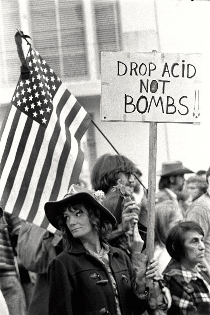 People protesting with a sign saying "Drop Acid, not Bombs!"